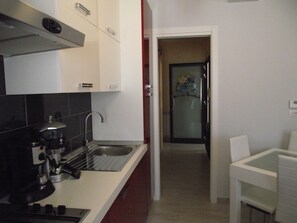Una cocina con cafetera, un lavamanos y armarios. Hay una puerta que da a una habitación con refrigerador y un letrero que dice "Tengo un bed and breakfast".