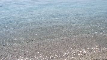 On aperçoit clairement une plage de galets, avec des bateaux au loin.