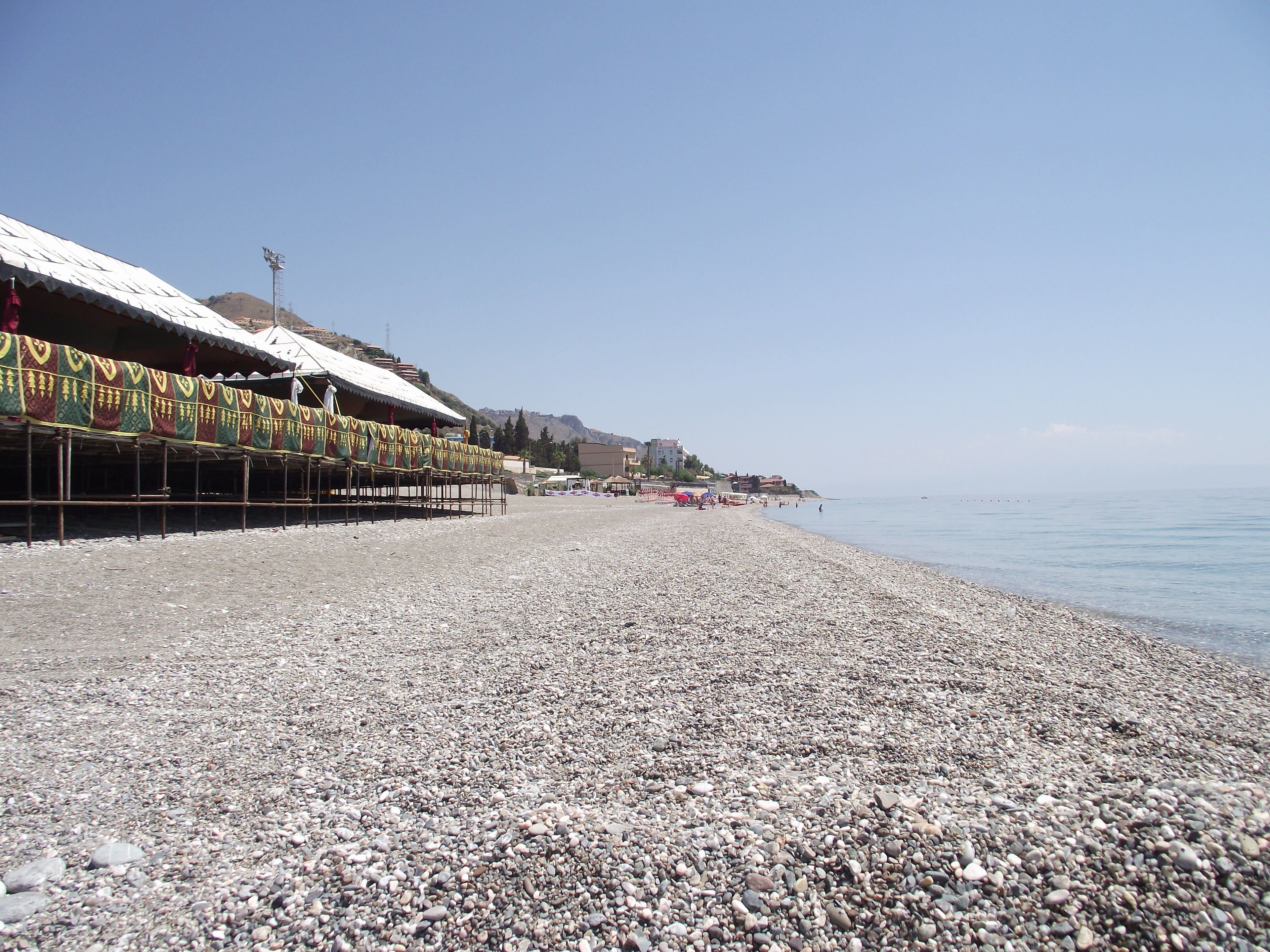 Ein Kiesstrand mit einer Reihe farbenfroher, traditioneller Gebäude am linken Ufer.