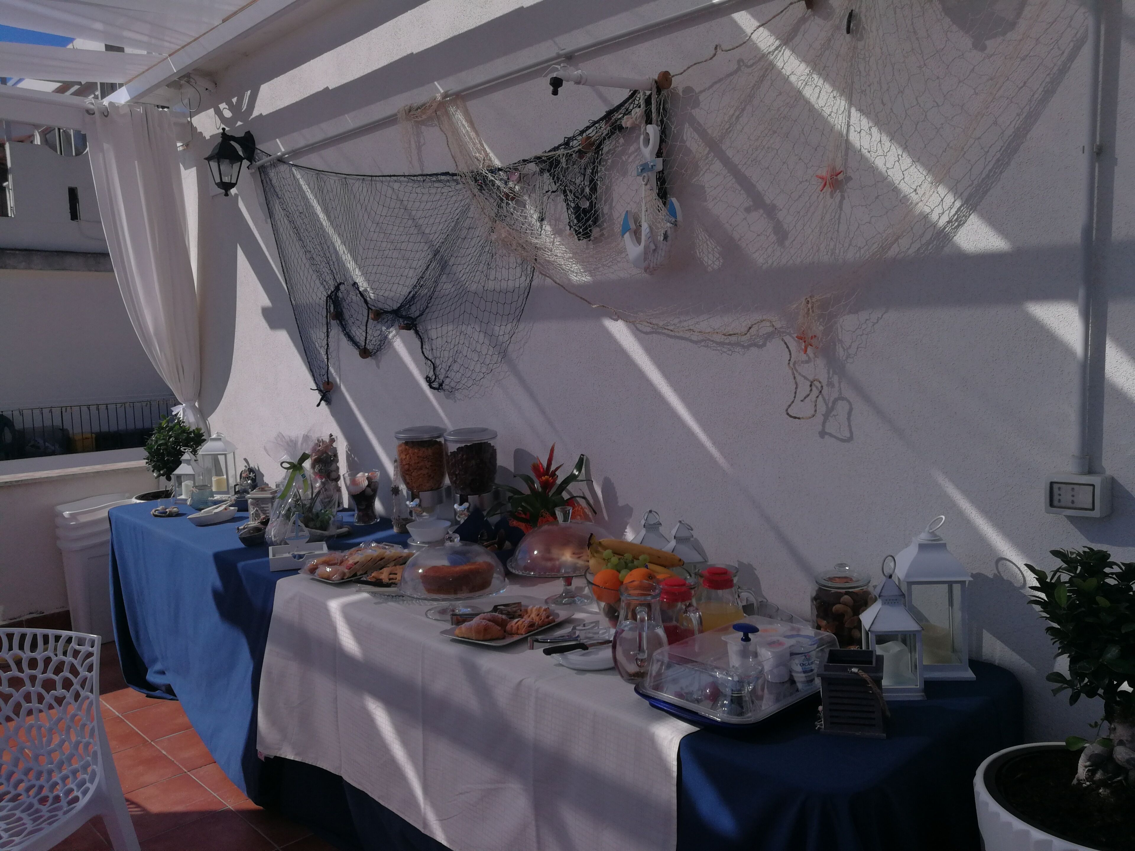 A table set up with various food items and drinks, a potted plant, and a decorative net hanging on the wall.