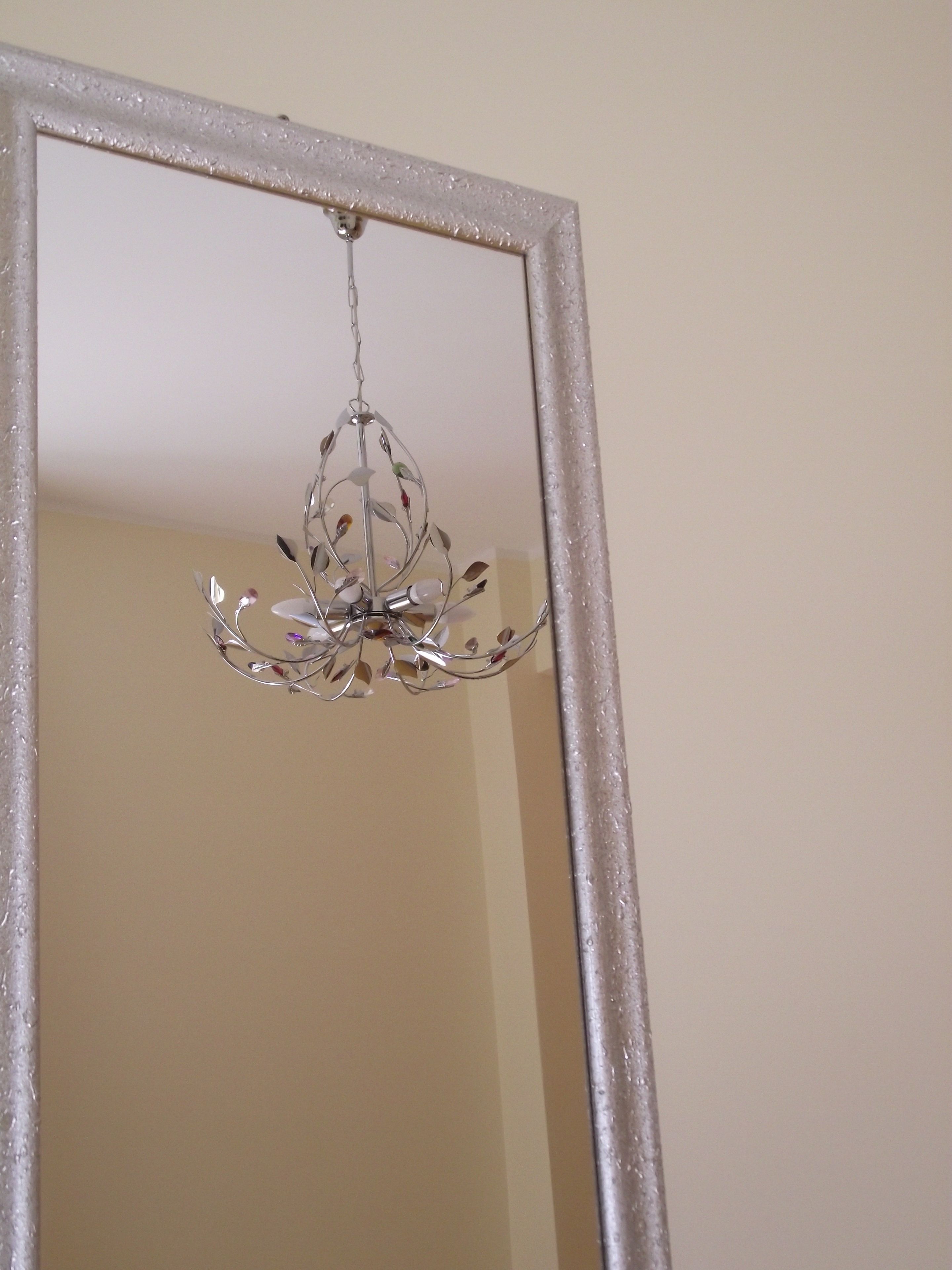 A mirror with a decorative metal frame and a hanging chandelier.