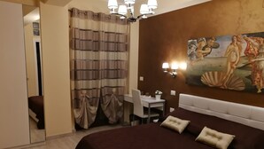 A hotel room with a large bed, a desk, and a chair. There is a painting on the wall and a chandelier. - B&B Il Mare degli Dei (Letojanni)