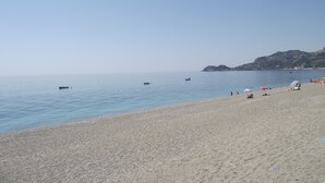 A beach with calm waters, a few boats, and people relaxing on the sand. - B&B Il Mare degli Dei (Letojanni)