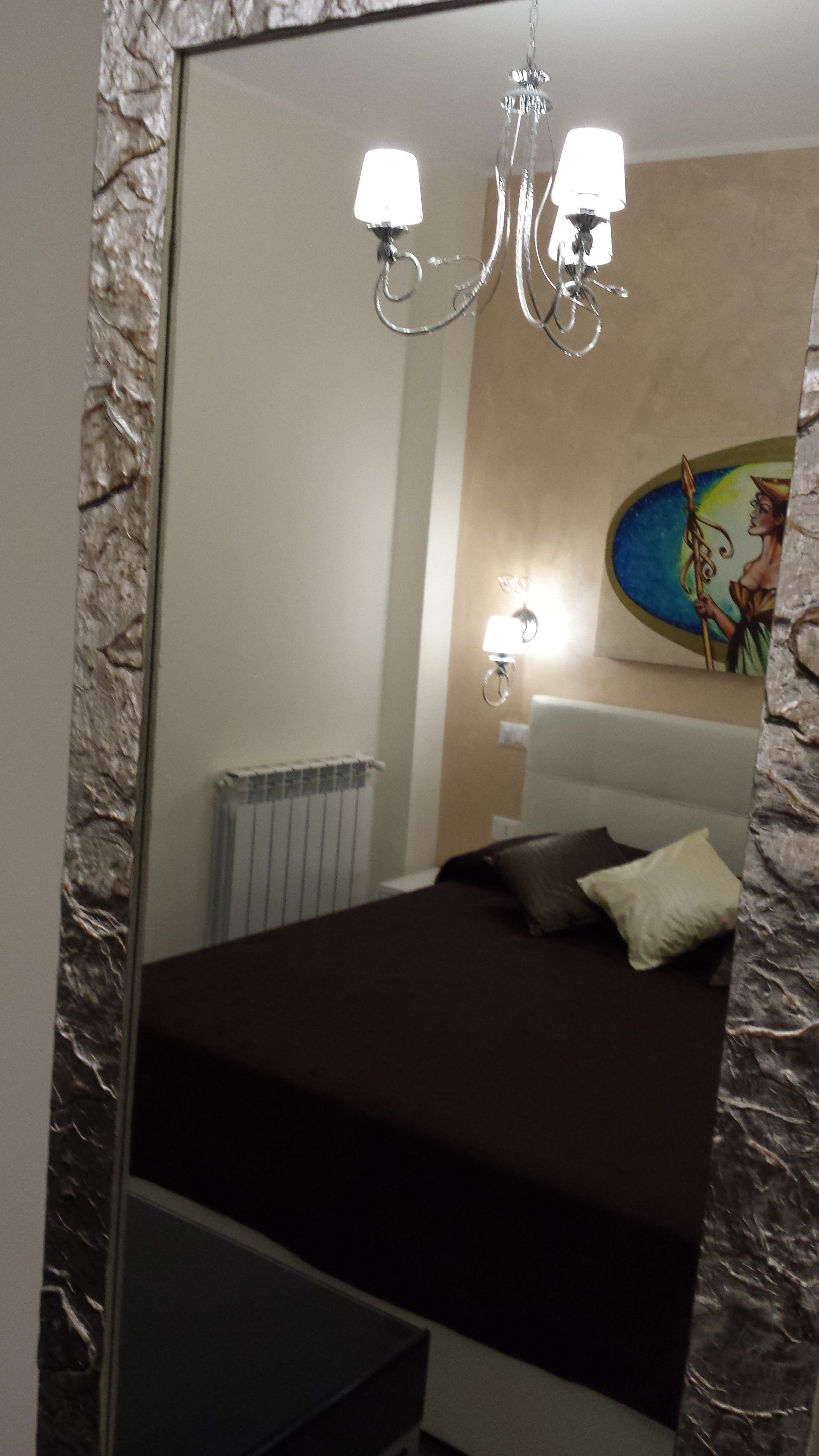 A bedroom with a large bed, a chandelier, a radiator, and a painting on the wall.