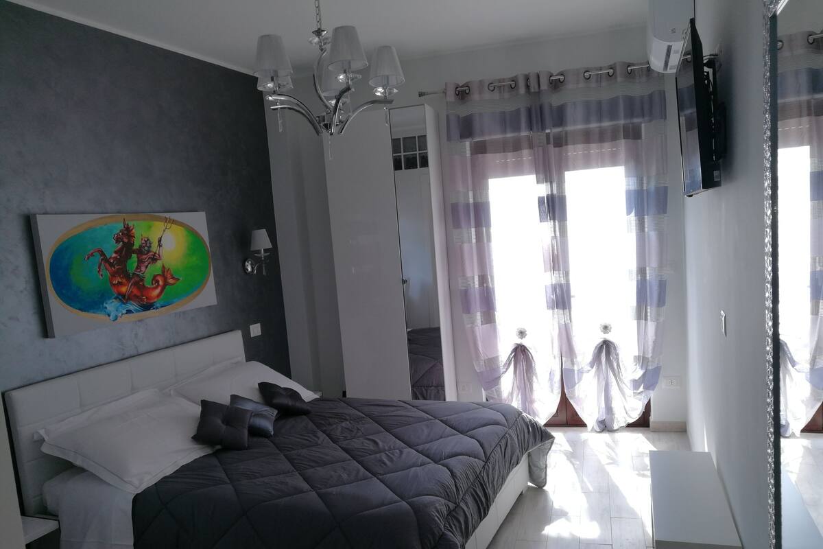 Une chambre avec un grand lit, un tableau au mur et une fenêtre avec des rideaux.