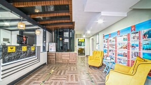 Un hall d’hôtel avec un comptoir d’accueil, un plancher en bois, des chaises jaunes et un mur orné d’affiches de voyage.