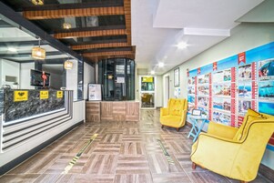 Un hall de hotel con mostrador de recepción, suelo de madera, sillas amarillas y una pared con carteles de viaje.