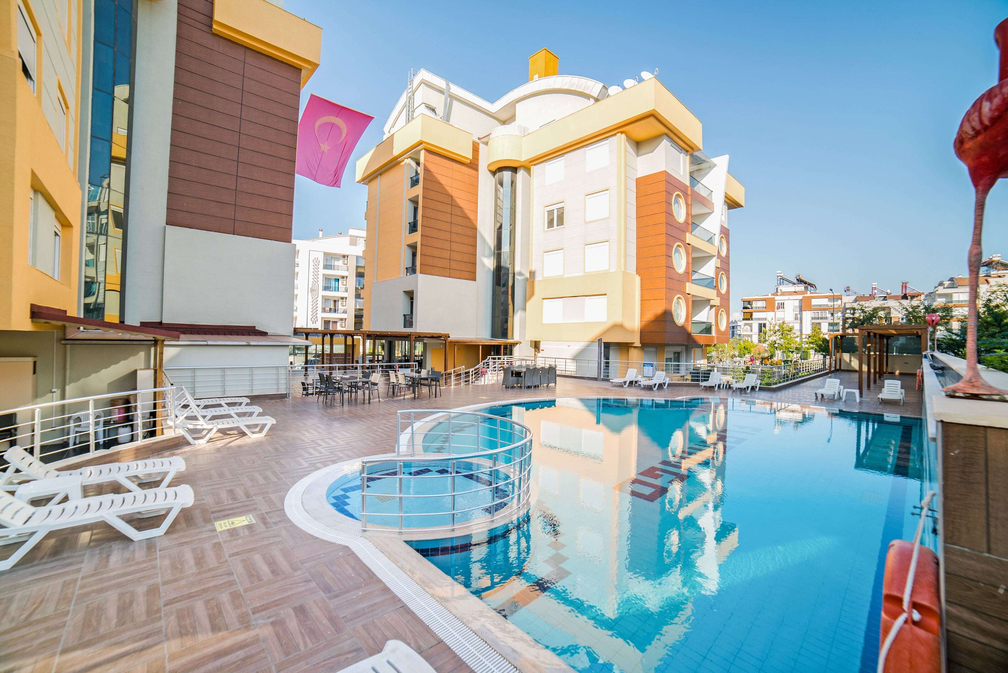 A rooftop swimming pool with lounge chairs and a sun deck, surrounded by modern buildings.
