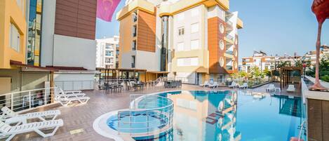 A rooftop swimming pool with lounge chairs and a sun deck, surrounded by modern buildings.
