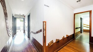 Un pasillo con suelo de madera, una serie de cuadros enmarcados en la pared y un espejo que refleja el pasillo.