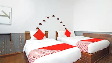 A hotel room with two beds, each with white bedding and red accents. The room has wooden flooring and a white wall with a decorative arch design.