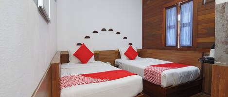 A hotel room with two wooden beds, white bedding, red pillows, and a wooden headboard with a unique design.
