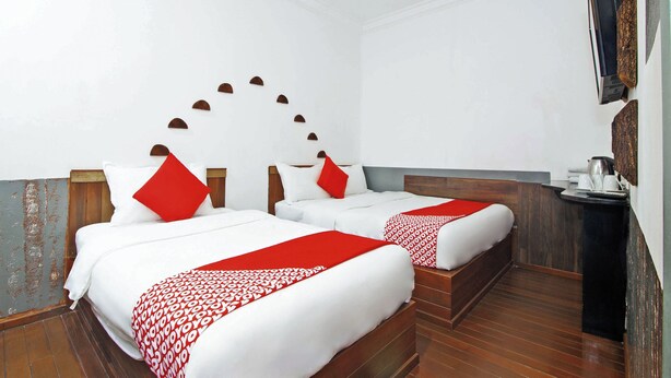 Habitación de hotel con dos camas, cada una con ropa de cama blanca y detalles rojos, suelo de madera y cafetera de pared.