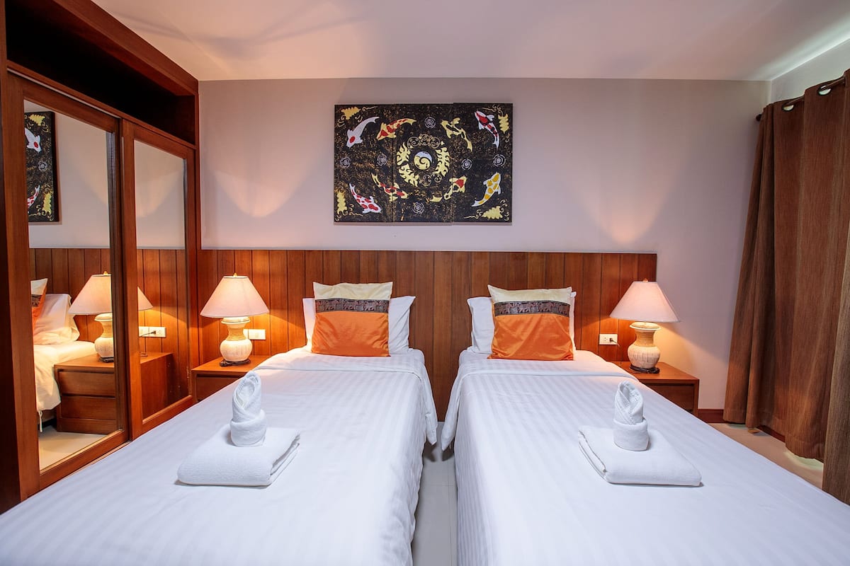 Een hotelkamer met twee bedden, houten hoofdeinden, bedlampen, een grote spiegel en een schilderij aan de muur.