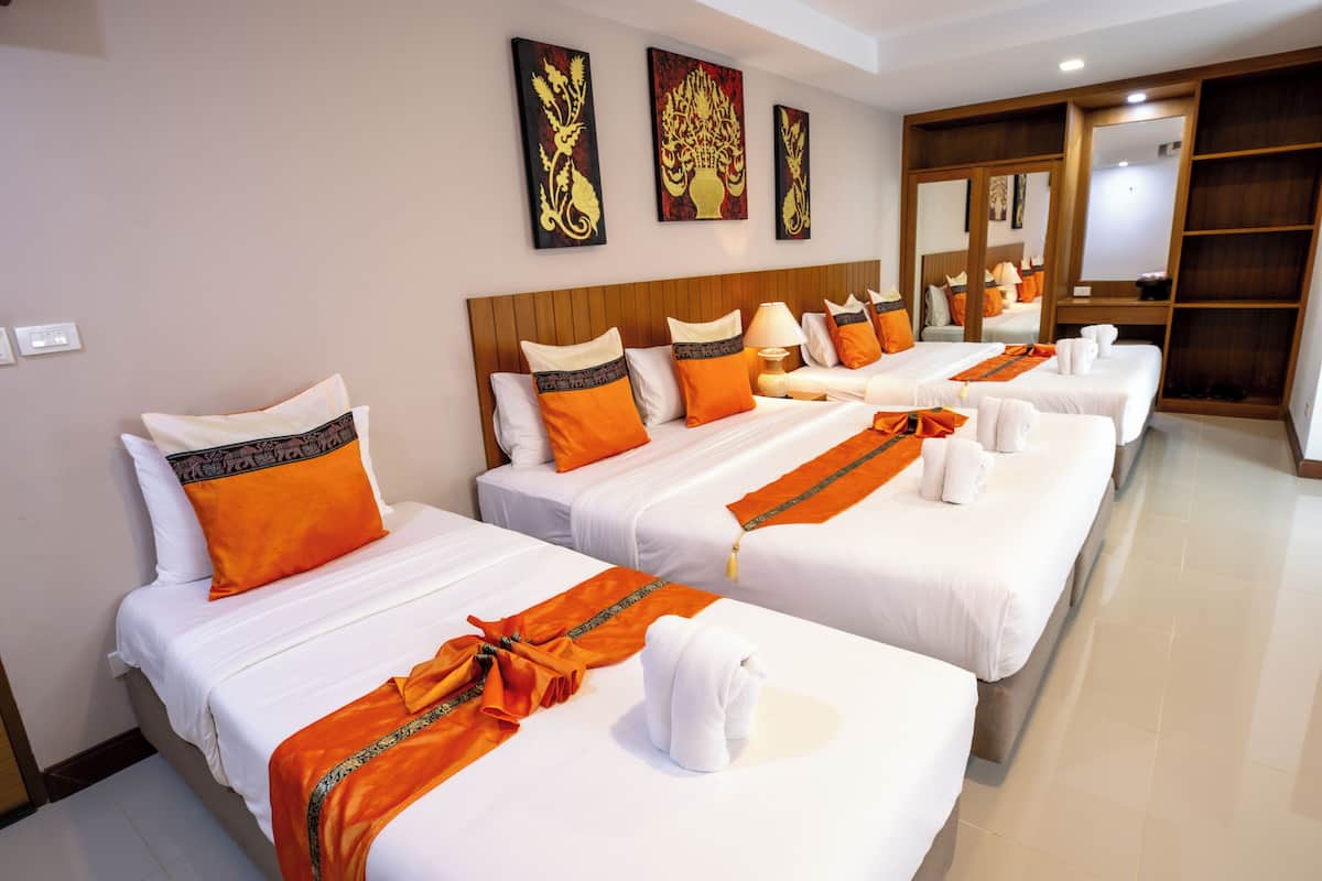 Een hotelkamer met drie bedden, elk voorzien van witte lakens en oranje accenten, een houten hoofdbord en kunst aan de muur.