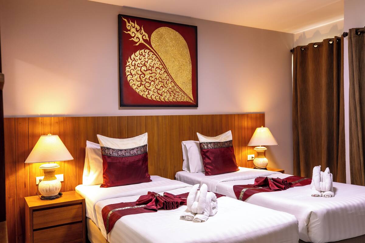 Een hotelkamer met twee bedden, elk voorzien van een rood-wit kussen, een houten hoofdbord en een wandlamp.