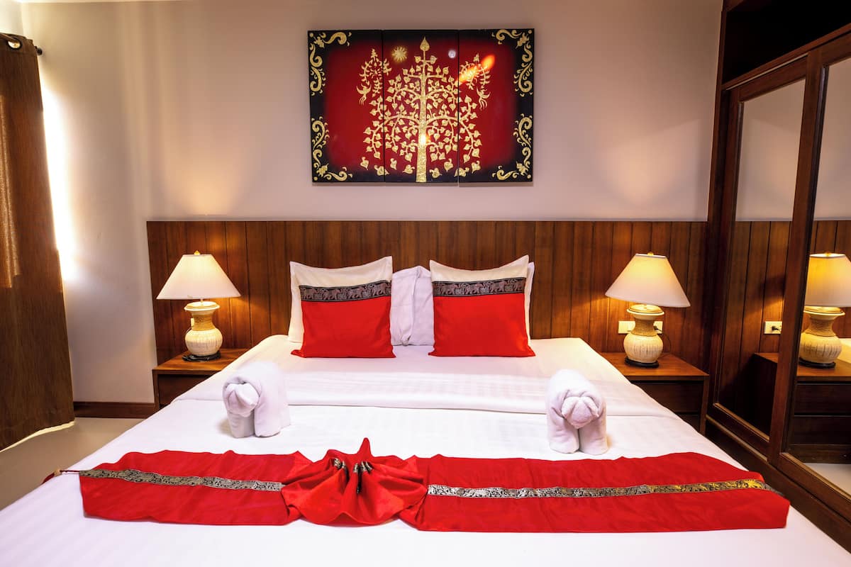 Een hotelkamer met een groot bed, twee bedlampen, een decoratieve wandversiering en een spiegel.