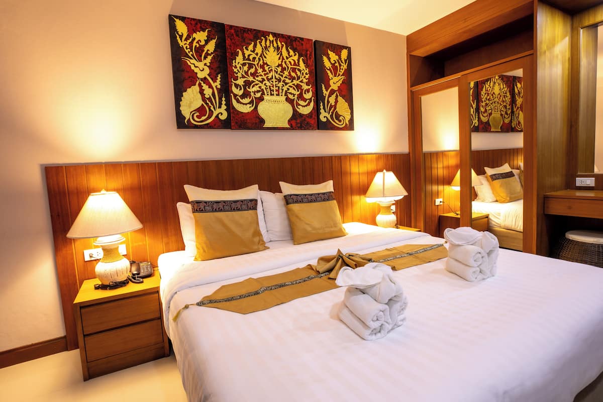Een hotelkamer met een groot bed, twee nachtkastjes met lampen, een spiegel en een decoratief schilderij aan de muur.