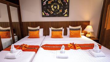 A hotel room with two beds, each with white linens and orange pillows. There is a painting on the wall above the beds, a nightstand with a lamp, and a wooden headboard.