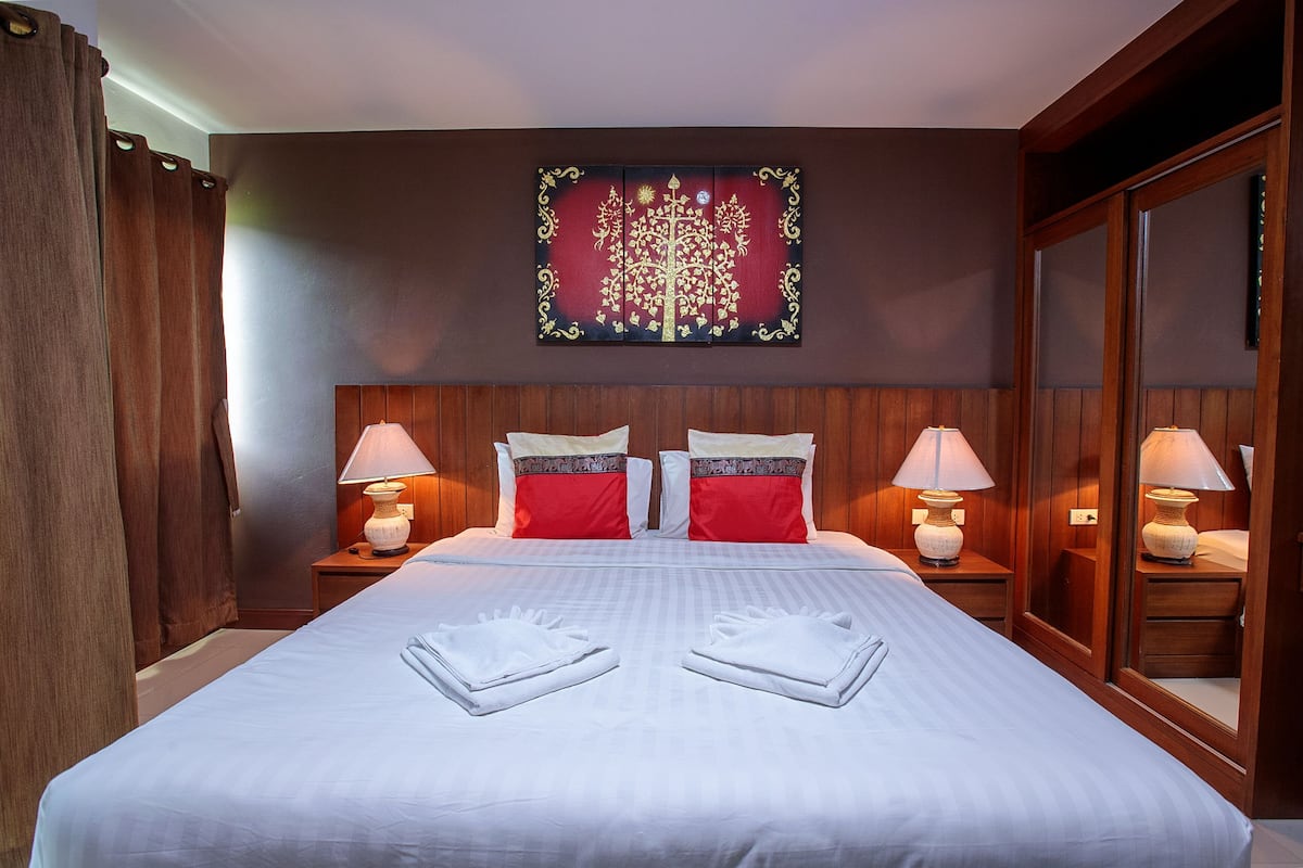 Een hotelkamer met een groot bed, twee nachtkastjes met lampen, een spiegel en een decoratief wandobject.