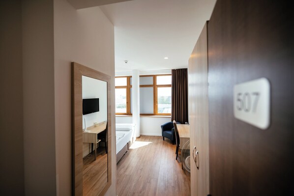 A hotel room with a bed, a desk, a chair, a TV, and a window with curtains.