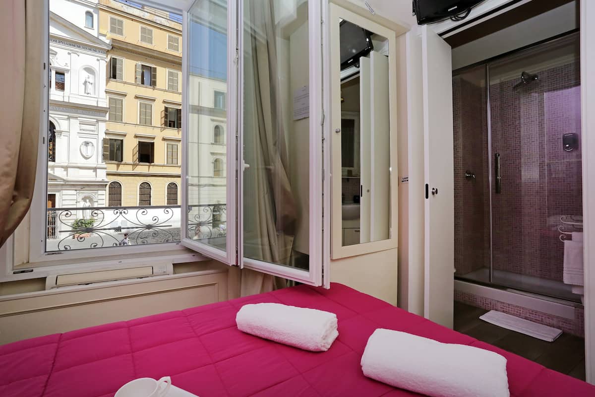 Ein Hotelzimmer mit Bett, einem Fenster mit Blick auf Gebäude und einer Duschkabine.