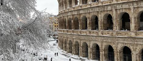 A snow-covered coliseum with multiple arches and a large tree in the foreground.