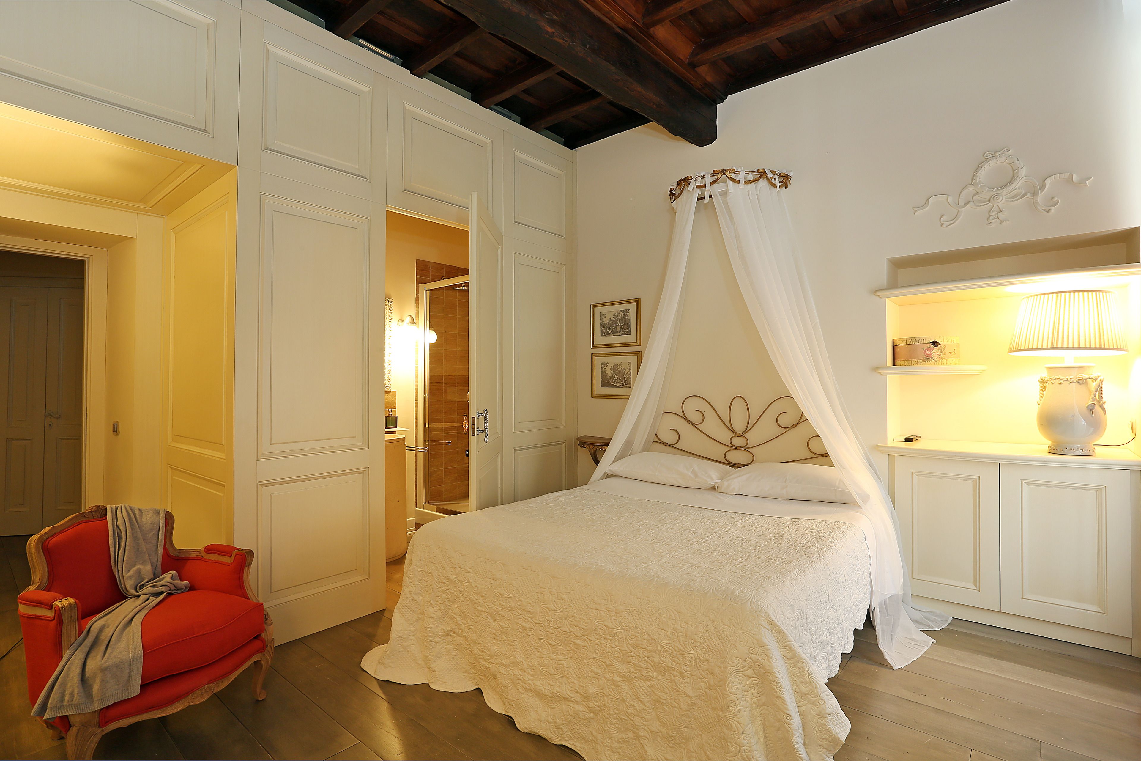 Un dormitorio con una cama con dosel, un sillón rojo y un armario blanco.