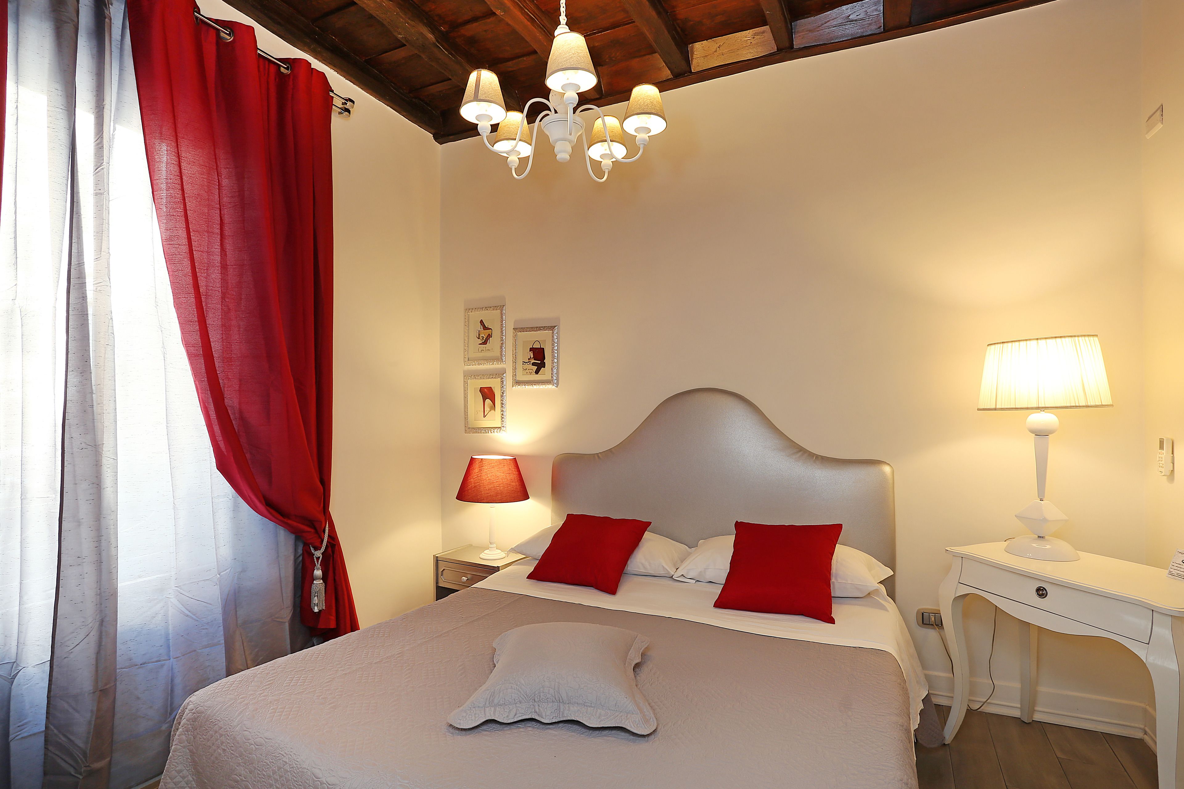 A neatly made bed with red and white pillows, a bedside lamp, and a small table with a lamp.