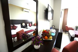 A hotel room with a bed, a desk with a vase of flowers, a fruit plate, and a television mounted on the wall. - Huong Son Hotel (Da Nang)