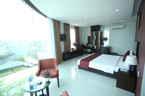 A modern hotel room with a large bed, a sitting area with a chair and table, a TV, and a balcony with a view of the city. - Huong Son Hotel (Da Nang)