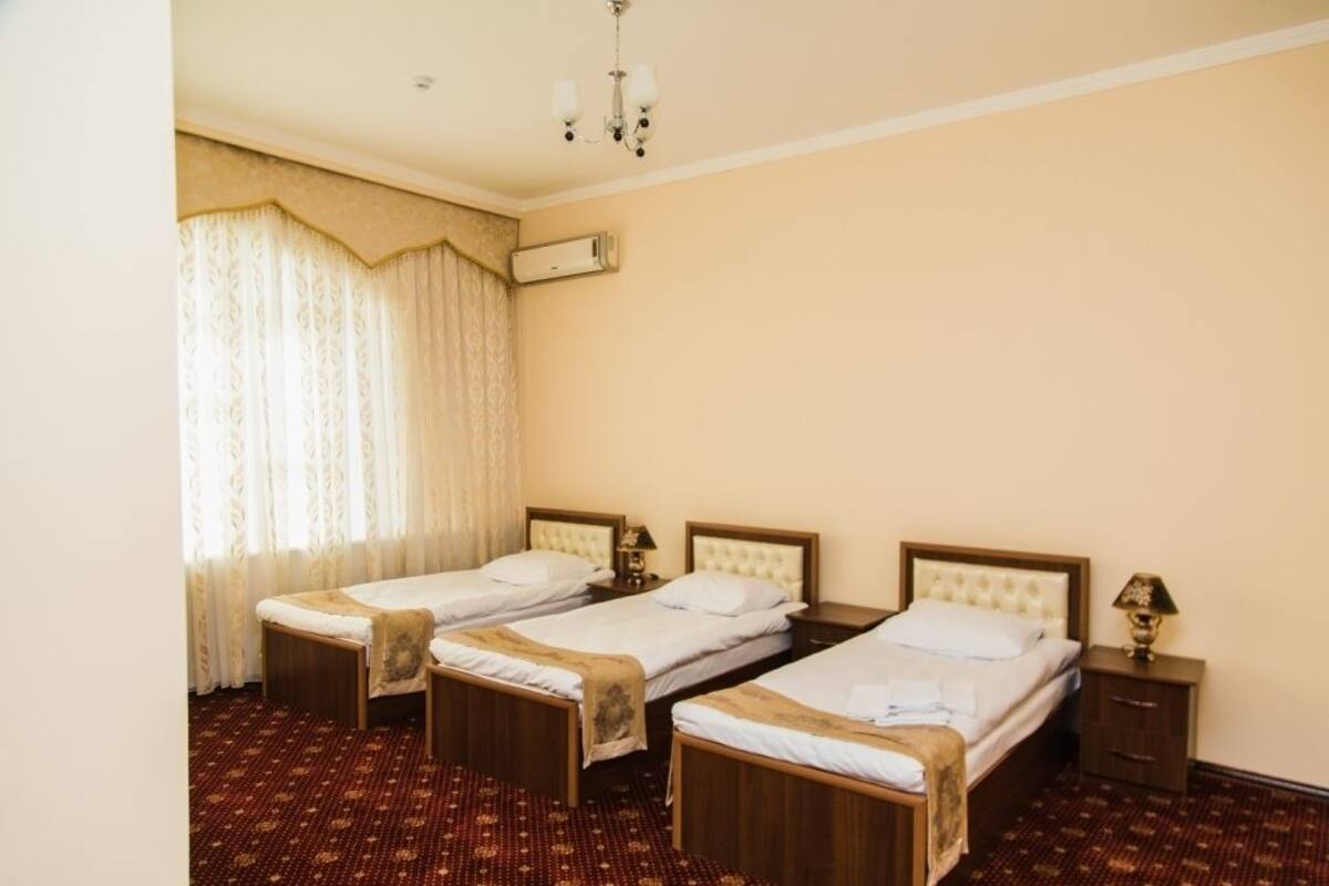 A hotel room with two single beds, a large window with curtains, a ceiling fan, and a wall-mounted air conditioner.