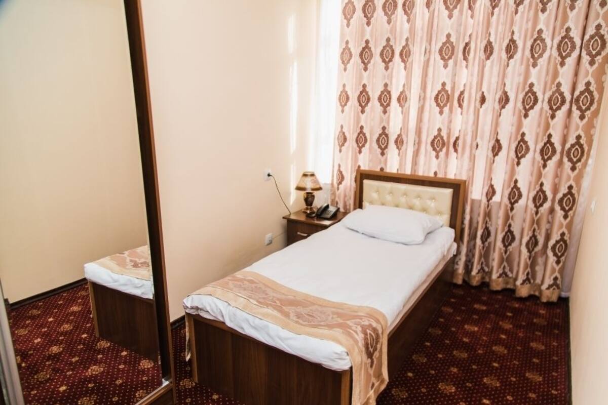 A hotel room with a single bed, a bedside table with a lamp, and a mirror.