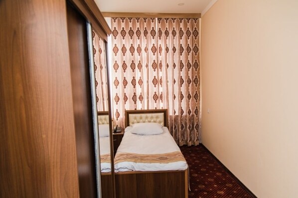 A hotel room with a single bed, a wooden headboard, a bedside table, and a patterned curtain.