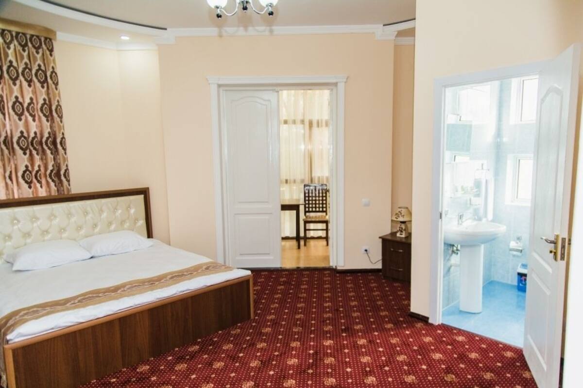 A hotel room with a bed, a red patterned carpet, a white door, and a bathroom with a sink.