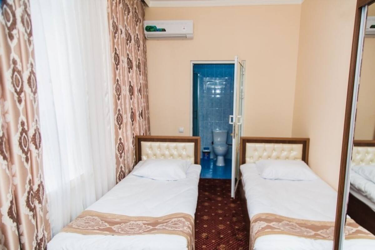 A hotel room with two beds, a bathroom with a blue-tiled shower, and an air conditioning unit on the wall.