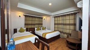 A hotel room with two beds, a wooden table, a chair, a TV, and a water bottle. - Mala Suites Thamel (Kathmandu)