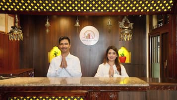 A reception desk with a logo for 'Mala Suites Thamel' and decorative elements like hanging bells and a plant.