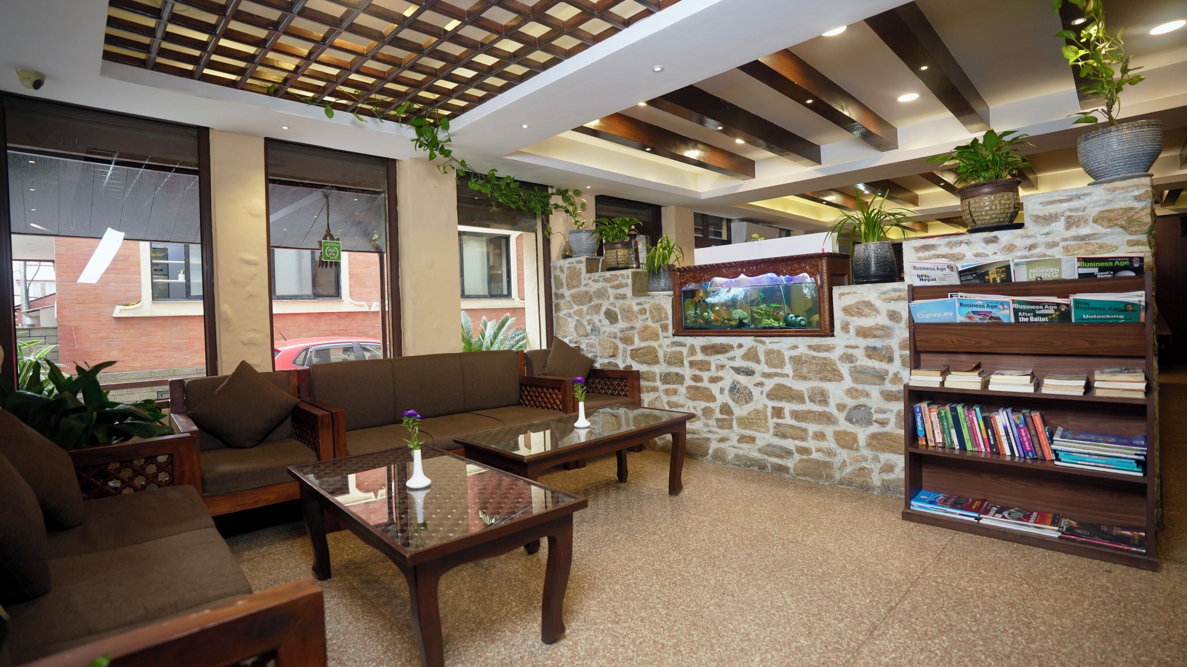 Un área de descanso moderna con pared de piedra, estantería con libros de negocios y un ventanal con vistas al exterior.