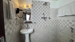 A bathroom with a white pedestal sink, a mirror, a towel rack, and a shower area with a glass-enclosed shower. - Mala Suites Thamel (Kathmandu)