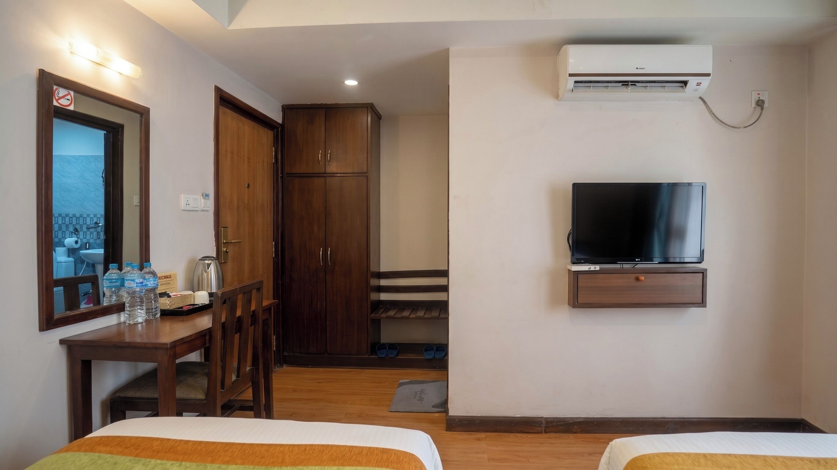A hotel room with a bed, a TV, a wardrobe, a desk with a mirror, and an air conditioning unit.