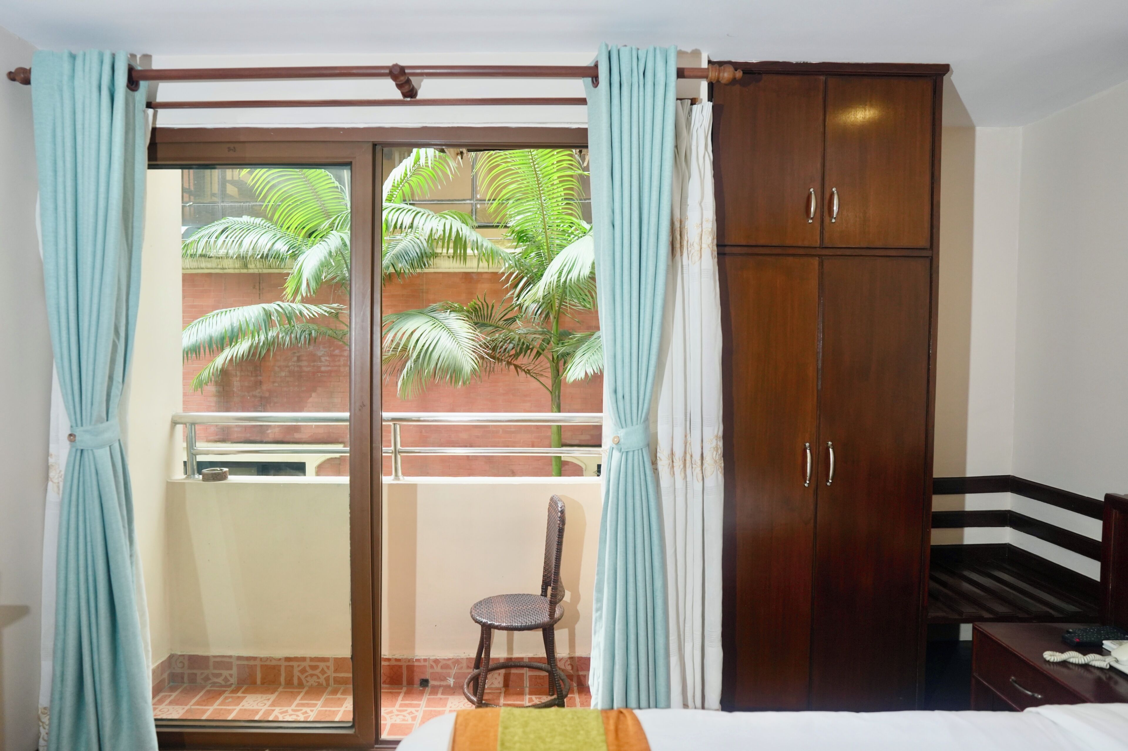 Una habitación con una cama, un armario de madera, una silla y un balcón con cortinas.