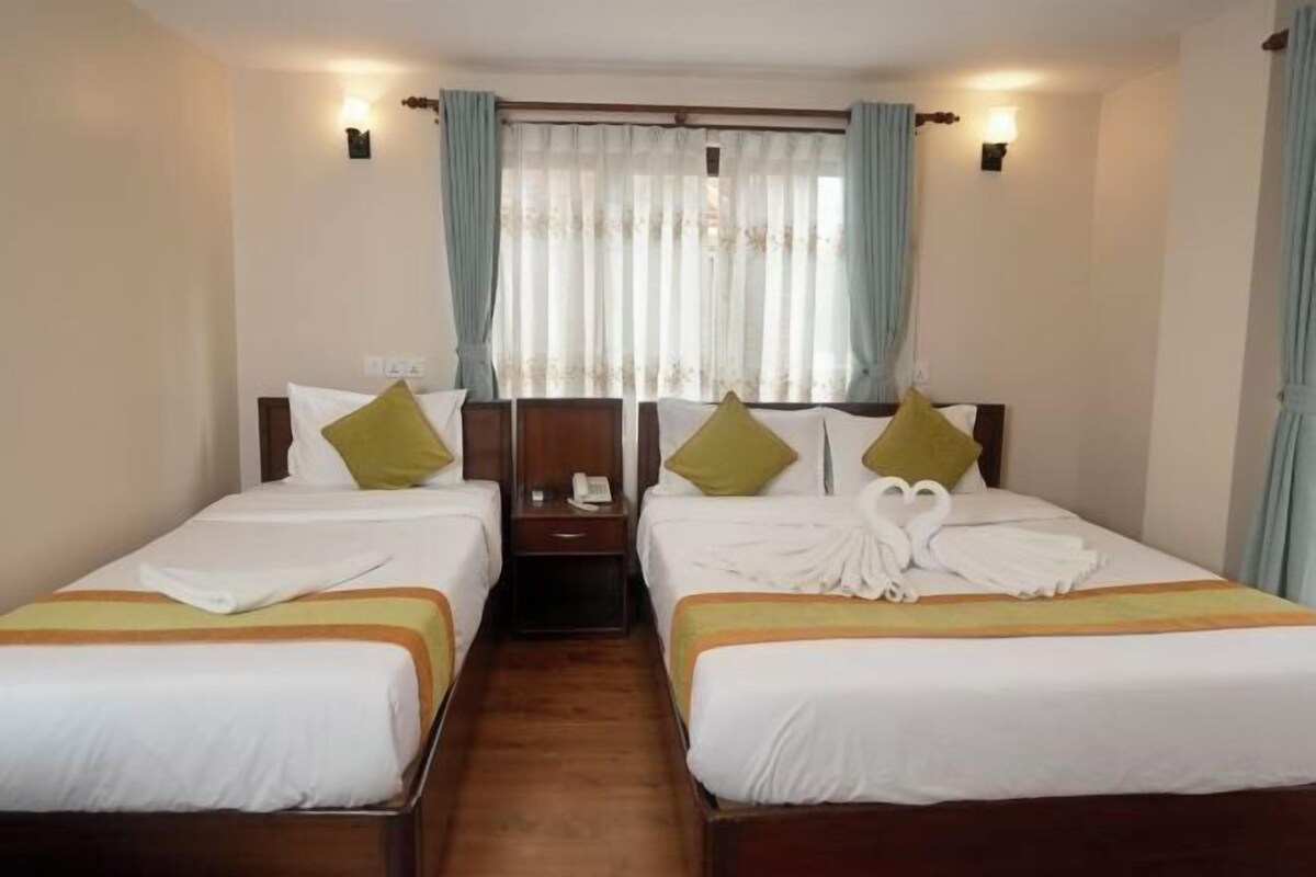 A hotel room with two single beds, a nightstand, and a window with curtains.