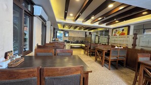 A restaurant with wooden tables and chairs, a kitchen area, and a large window. - Mala Suites Thamel (Kathmandu)