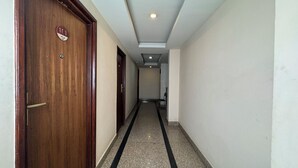 Um corredor estreito com portas de madeira em uma lateral e chão de azulejos.