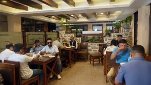 Eine Gruppe von Menschen speist in einem Restaurant mit Holztischen und Steinsäulen.
