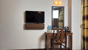 A hotel room with a flat-screen TV mounted on the wall, a wooden desk with two water bottles, and a mirror reflecting part of the room. - Mala Suites Thamel (Kathmandu)