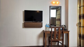A hotel room with a flat-screen TV mounted on the wall, a wooden desk with two water bottles, and a mirror reflecting part of the room. - Mala Suites Thamel (Kathmandu)