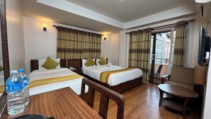 A hotel room with two beds, a wooden table, a chair, a TV, and a balcony with a chair. - Mala Suites Thamel (Kathmandu)