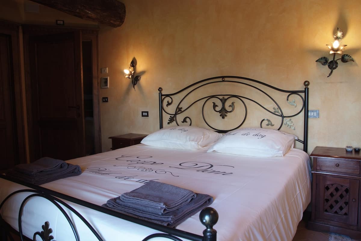 A neatly made bed with a metal headboard, a bedside table with a lamp, and a wall-mounted light fixture.